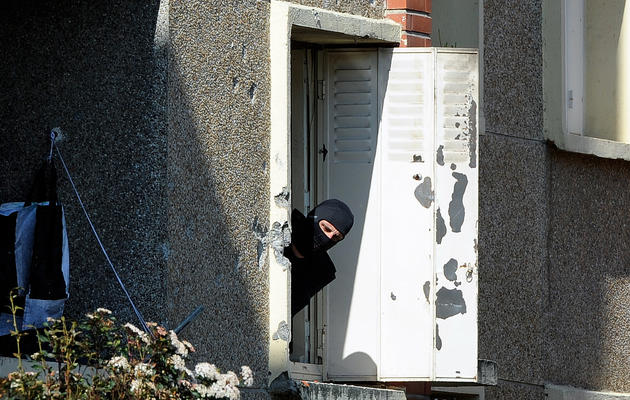 un homme encagoulé regarde par la fenêtre de l'appartement de Mohamed Merah, à toulouse, le 23 mars 2012 [Jean-Pierre Muller / AFP]