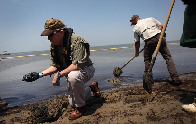 Des personnes retirent du pétrole d'une plage de Louisiane, le 19 avril 2011, un an après la marée noire dans le Golfe du Mexique [John Moore / Getty Images/AFP/Archives]