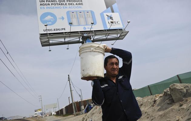 Un homme transporte un baquet d'eau près d'un panneau publicitaire qui convertit l'humidité de l'air en eau potable, à Bujama au Pérou le 15 mars 2013 [Ernesto Benavides / AFP/Archives]