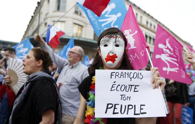 Une manifestante masquée tient une affichette demandant à François Hollande d'écouter son peuple le 17 avril 2013 à Paris [Kenzo Tribouillard / AFP]