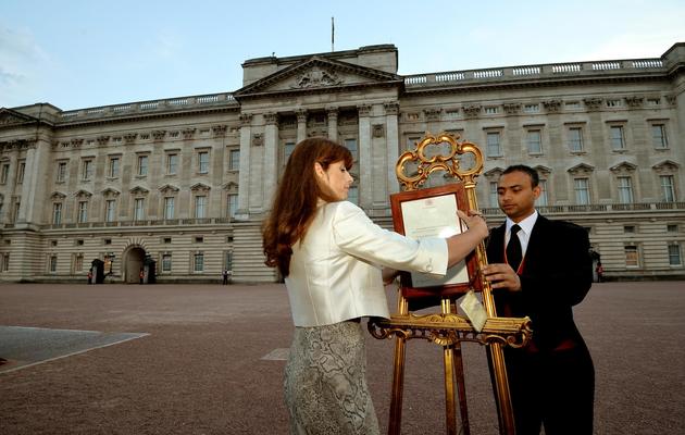 Des membres du service de presse de la Reine placent un écriteau devant le palais de Buckingham pour annoncer la naissance du fils de la Duchesse de Cambridge et du Prince William le 22 juillet 2013 à Londres [ / POOL/AFP]