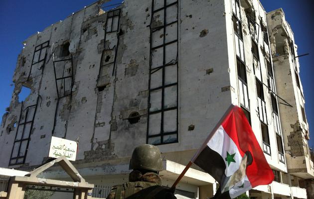 Un soldat de l'armée syrienne tient un drapeau sur lequel est imprimé un portrait du président Bachar al-Assad devant un bâtiment en ruine, le 5 juin 2013 à Qousseir [- / AFP/Archives]