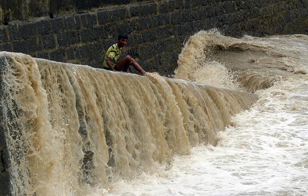 Un garçon assis sur un muret d'où s'écoulent des trombes d'eau le 25 juin 2013 à Bombay [ / AFP]