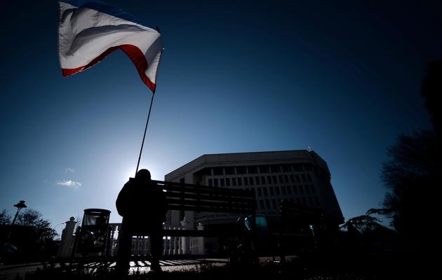 Un homme assis sur un banc brandissant un drapeau de Crimée devant le parlement de Crimée à Simféropol le 18 mars 2014 [Filippo Monteforte / AFP]