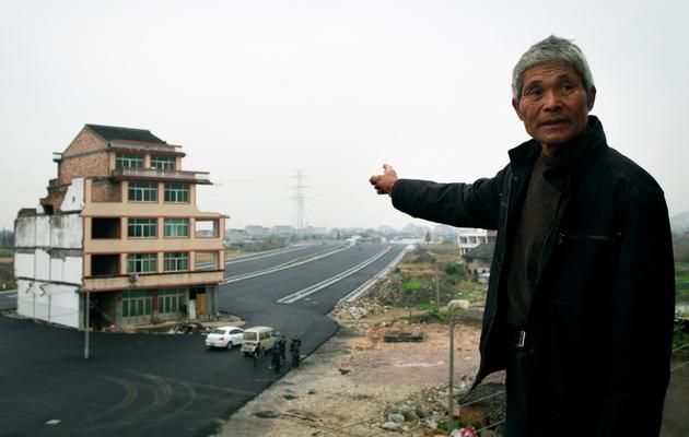 Luo Baogen, 67 ans, montre l'immeuble d'où il refuse de partir avec sa femme et qui se retrouve au milieu d'une route, le 22 novembre 2012 [ / AFP]