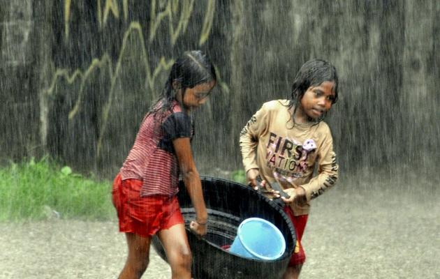 Des enfants transportent une bassine sous la pluie battante, le 2 janvier 2013 à Dili [Valentino de Sousa / AFP]